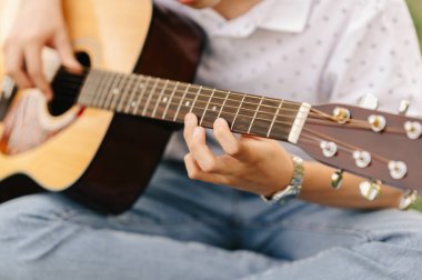 Parkta oturan bir gencin akustik gitar çalmayı öğrenmesini yakından çek..