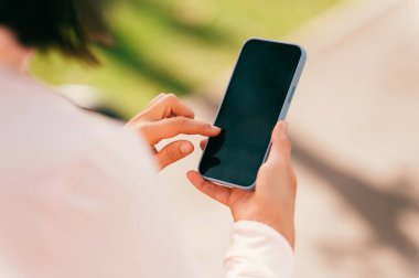 Orta yaşlı bir kadının dışarıda akıllı telefonunu kontrol ederken çekilmiş yakın plan fotoğrafı..
