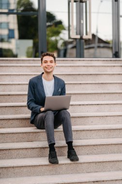 Uzaktan kumandayla çalışmak, genç bir ofis çalışanı dışarıda oturuyor ve dizüstü bilgisayar kullanıyor..