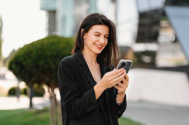 Neşeli genç iş kadını işe ara verirken elinde tuttuğu telefona bakıyor..