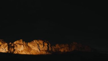 Gece vakti gökyüzü ve yıldızların devasa bir kayanın yanında çekilmiş zaman kaydı..