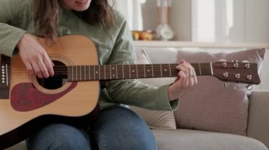 Evde akustik gitar çalan genç bir kadının görüntüsü..