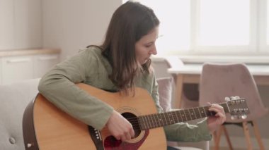 Evde akustik gitar çalan genç bir kadının görüntüsü..