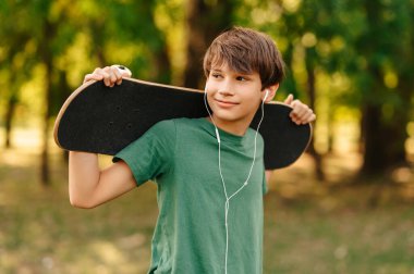 Kulaklıkla müzik dinleyen ve kaykayını tutan havalı bir gencin açık hava portresi..