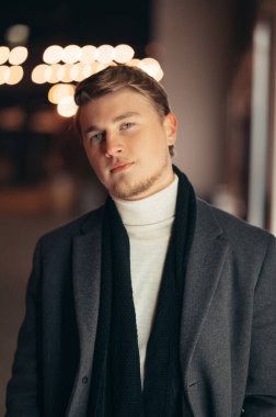 Arka planda ışıklar olan ceketli genç bir sarışının dikey portresi..