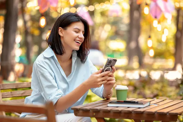 Cute young woman working remote from her phone while sitting at a cafe in park.