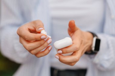 Akıllı saat takan, kablosuz kulaklığı ve beyaz çantasını tutan kadınların yakın çekimleri..