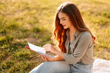 Güzel genç bayan öğrenciler çimenlerde oturuyor ve güneşli bir günde bir kitaptan öğreniyorlar..