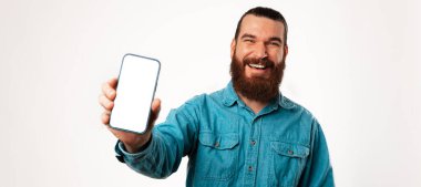 Mavi gömlekli genç adam cep telefonunu boş ekranlı tutuyor. Banner stüdyosu beyaz arkaplanda çekildi.