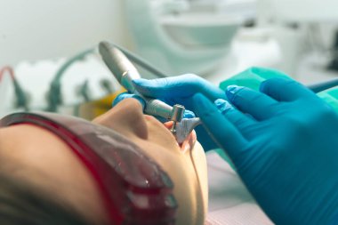 Diş hekimi, dişçi kliniğinde genç bir bayan hasta için profesyonel diş temizliği yapıyor..