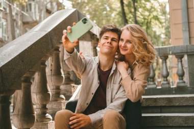 Genç aşıklar telefonda selfie çekerken ve dışarıda merdivenlerde otururken birlikte vakit geçiriyorlar..