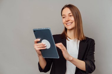 Ceket giyen genç akıllı kadın dijital tablet üzerinde çalışıyor. Stüdyo portresi gri arkaplan üzerinde.