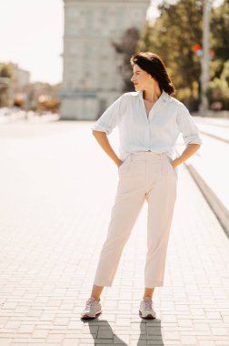 Güneşli bir günde elleri cebinde bekleyen genç bir kadının dikey dış görünüşü..