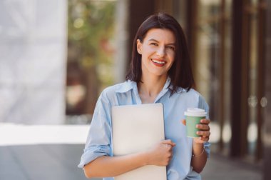 Gömlek giyen yakışıklı genç bayan dışarıda güzel bir kahvenin tadını çıkarırken bilgisayarını tutuyor..
