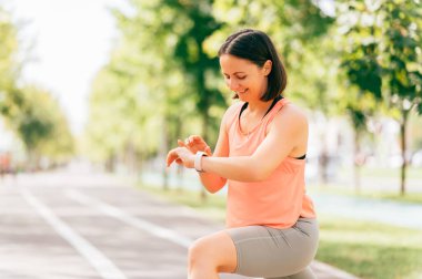 Orta yaşlı sporcu kadının açık hava portresi akıllı saat nabzını kontrol ediyor..