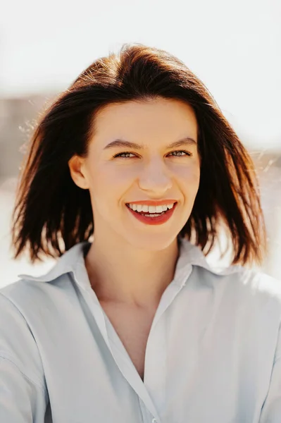 Close up vertical portrait of a wide smiling or laughing woman outdoors on a sunny day.