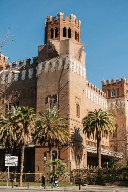 24 Şubat 2023, İspanya, Barselona. Güneşli bir günde Barcelona 'da tuğla bina ve palmiye ağaçlarının dikey açılışı..