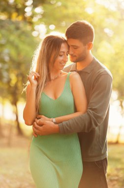 Aşık genç bir çiftin yazın gün batımında sarılışının dikey çekimi..