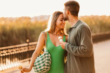 Açık havada, elinde dondurma tutarken sevgilisini öpen bir gencin fotoğrafı..