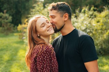 Güzel, mutlu bir çiftin, parkta yürürken kadınını öptüğü sıcak bir fotoğraf..