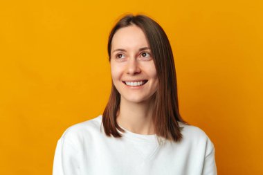 Sarı arka plana bakan gülümseyen genç bir kadının stüdyo portresini kapat.