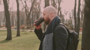 Sakallı hippi adamın park reklamında yürürken kahve içerken, kahveyi götürürken..