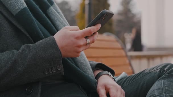 近景视频 男人坐在公园的长椅上 用智能手机 — 图库视频影像