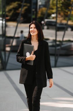 Elinde dizüstü bilgisayarı olan, dışarıda ceket giyen başarılı bir kadının dikey fotoğrafı..