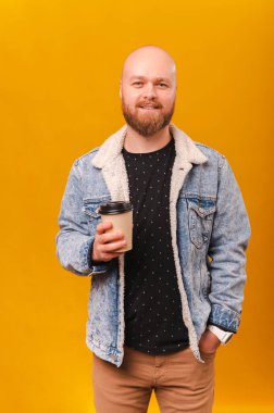 Sarı arka planda elinde kağıt bardakla gülümseyen kel bir adamın dikey çekimleri..