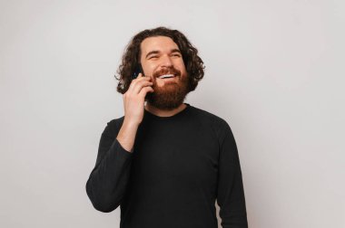 Genç, kendinden geçmiş, güçlü, sakallı bir adamın beyaz arka planda telefonla konuşması..