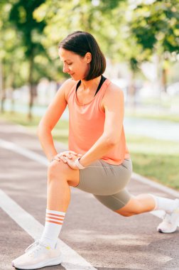 Güneşli bir günde koşmadan önce esneyen neşeli orta yaşlı bir kadının açık hava portresi..