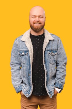 Sarı arka planda elleri cebinde gülümseyen kel bir adamın dikey çekimi..