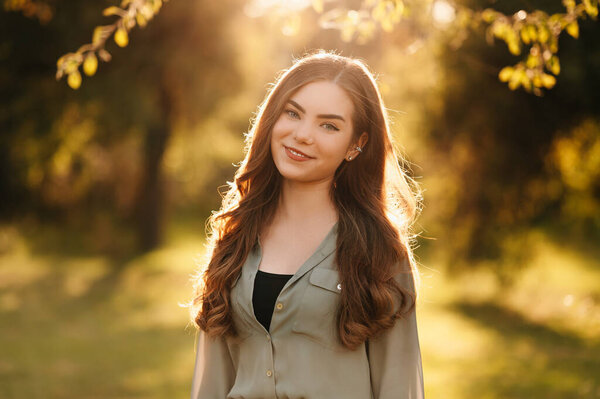 Портрет молодой улыбающейся женщины, стоящей в парке в солнечный день.
