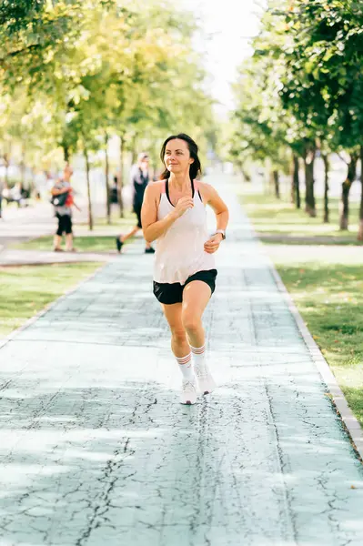 Vertical outdoors shot of mid age woman wearing sportswear running on the street.