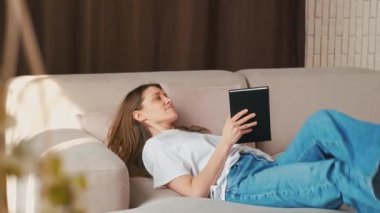 Kafkasyalı genç bir kadın kanepede uzanıp kitap okuyor, dinleniyor..