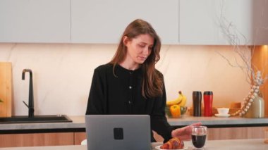 Uzaktan kumandayla mutfakta çalışan ve kahve içen genç bir kadının görüntüsü..