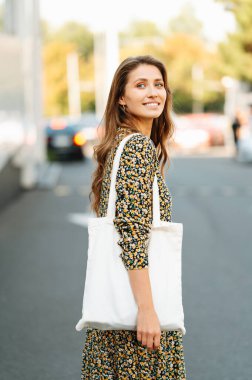 Elbise giymiş, çantasıyla yürüyen genç bir kadının dikey portresi..