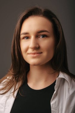 Gri arka planda gülümseyen genç bir kadının dikey stüdyosunu kapat..