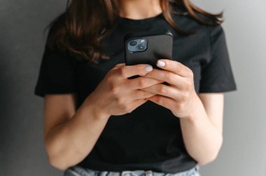 Siyah tişörtlü, akıllı telefonunu kullanan yüzsüz bir kadının fotoğrafı. Boşluğu kopyala.