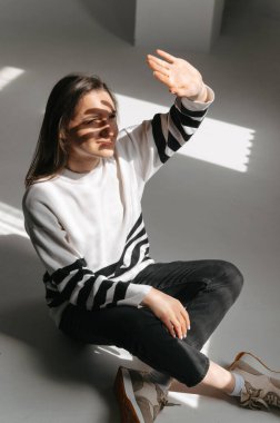 Bir kadının yerde otururken gün ışığının tadını çıkardığı uzun bir stüdyo fotoğrafı..