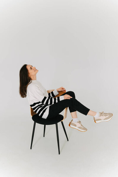 Полный снимок женщины, хорошо проводящей время, сидя на стуле в белой студии.