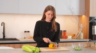 Ahşap kesme tahtasının üzerinde sarı biber dilimleyen beyaz bir kadın..