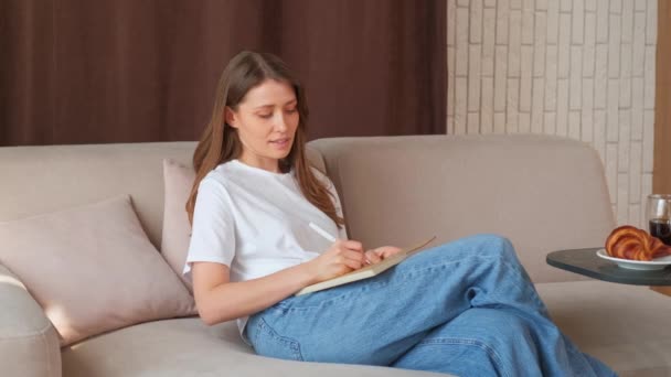 ソファーに座ってアジェンダを書いている若い女性のビデオ — ストック動画