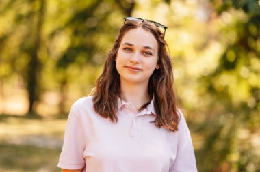 Yazın kameraya gülümseyen neşeli bir bayan öğrencinin açık hava portresini kapat..