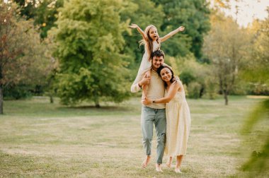 Üç kişilik neşeli aile parkta çimenlerde yürürken birlikte vakit geçiriyorlar..