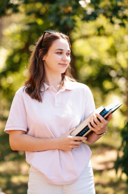 Beyaz giyen neşeli bayan öğrenci kampüste yürürken kitaplarını taşıyor..