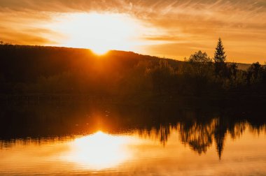 Açık hava manzarası, günbatımında yanında ağaçlar olan küçük bir gölün sakin görüntüsü..