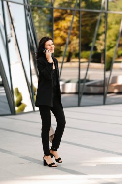 Genç, başarılı, kendine güvenen bir kadın dışarıda yürürken telefonla konuşuyor..