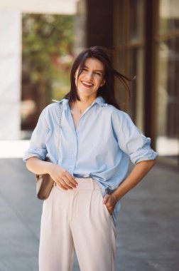 Genç esmer, neşeli kadın dışarıda durup gülümsüyor ve hayatın tadını çıkarıyor..