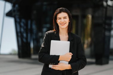 Genç ve başarılı bir kadın, güneşli bir günde dizüstü bilgisayarını açık havada tutuyor..